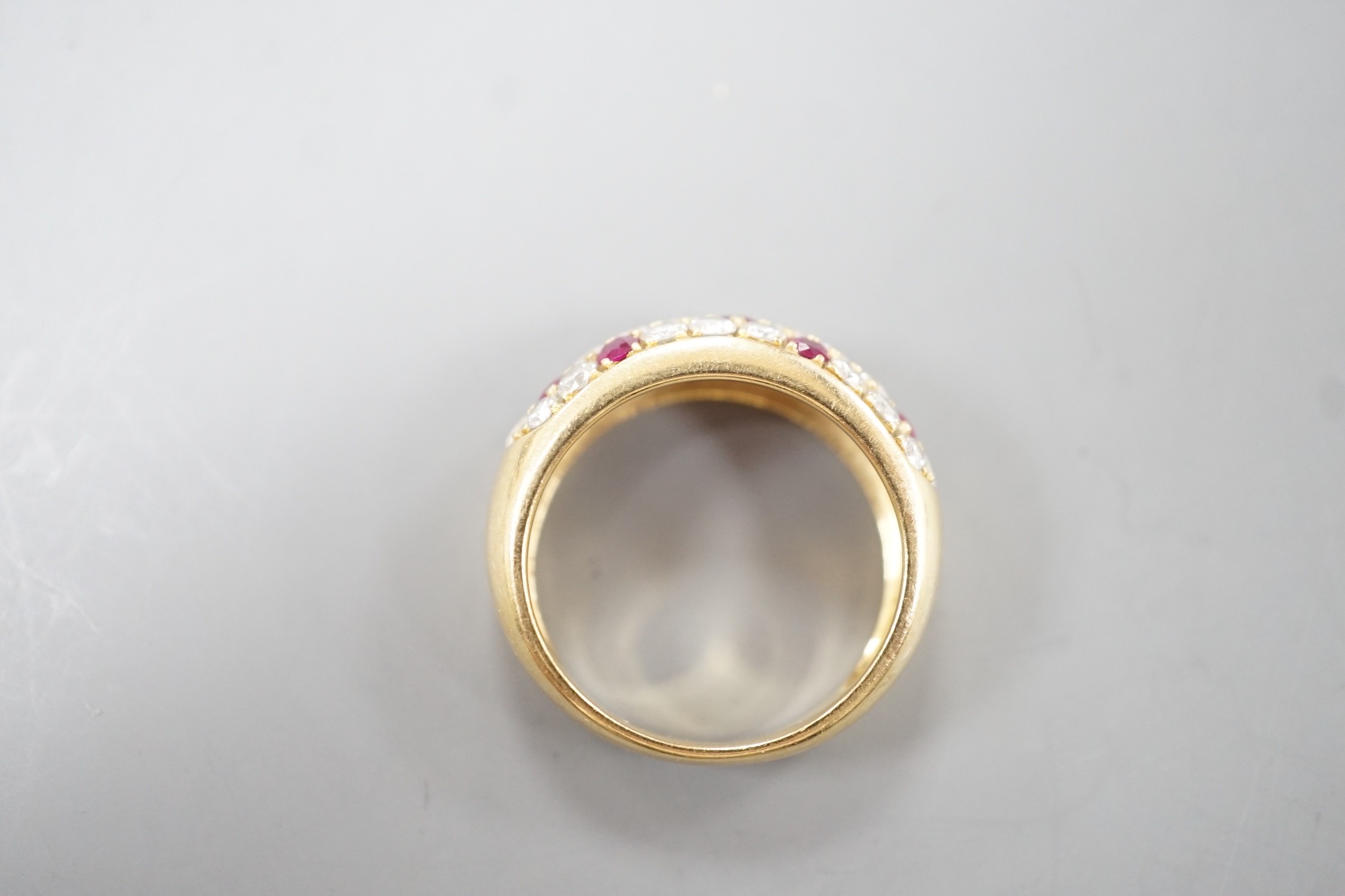 A modern yellow metal, ruby and diamond cluster set half hoop ring, size L/M, gross weight 4.5 grams.